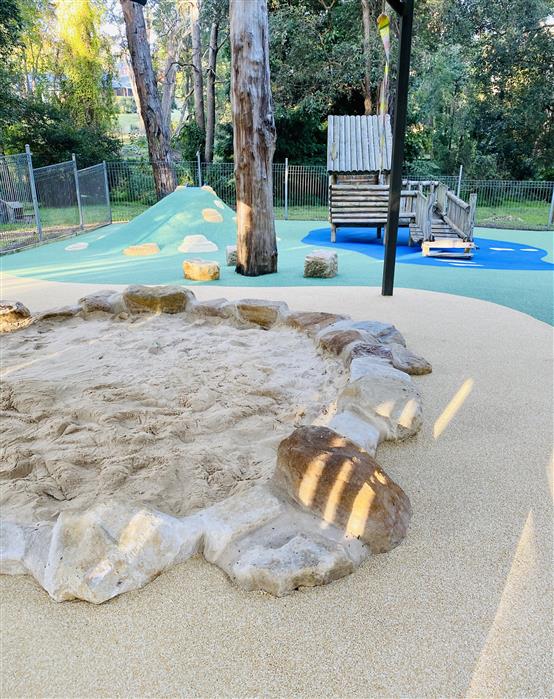 Nature play garden with mulch, rocks, tree stumps and leafy plants at The Discovery House